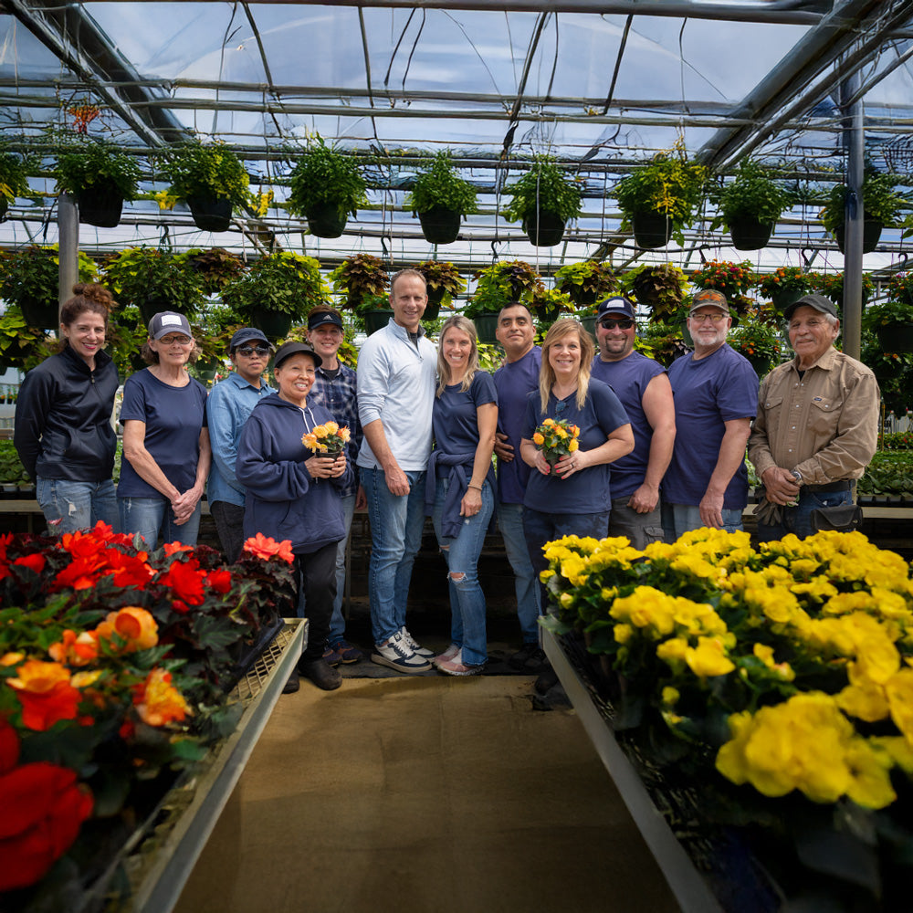 Group of people posing in a greenhouse with plants and flowers around